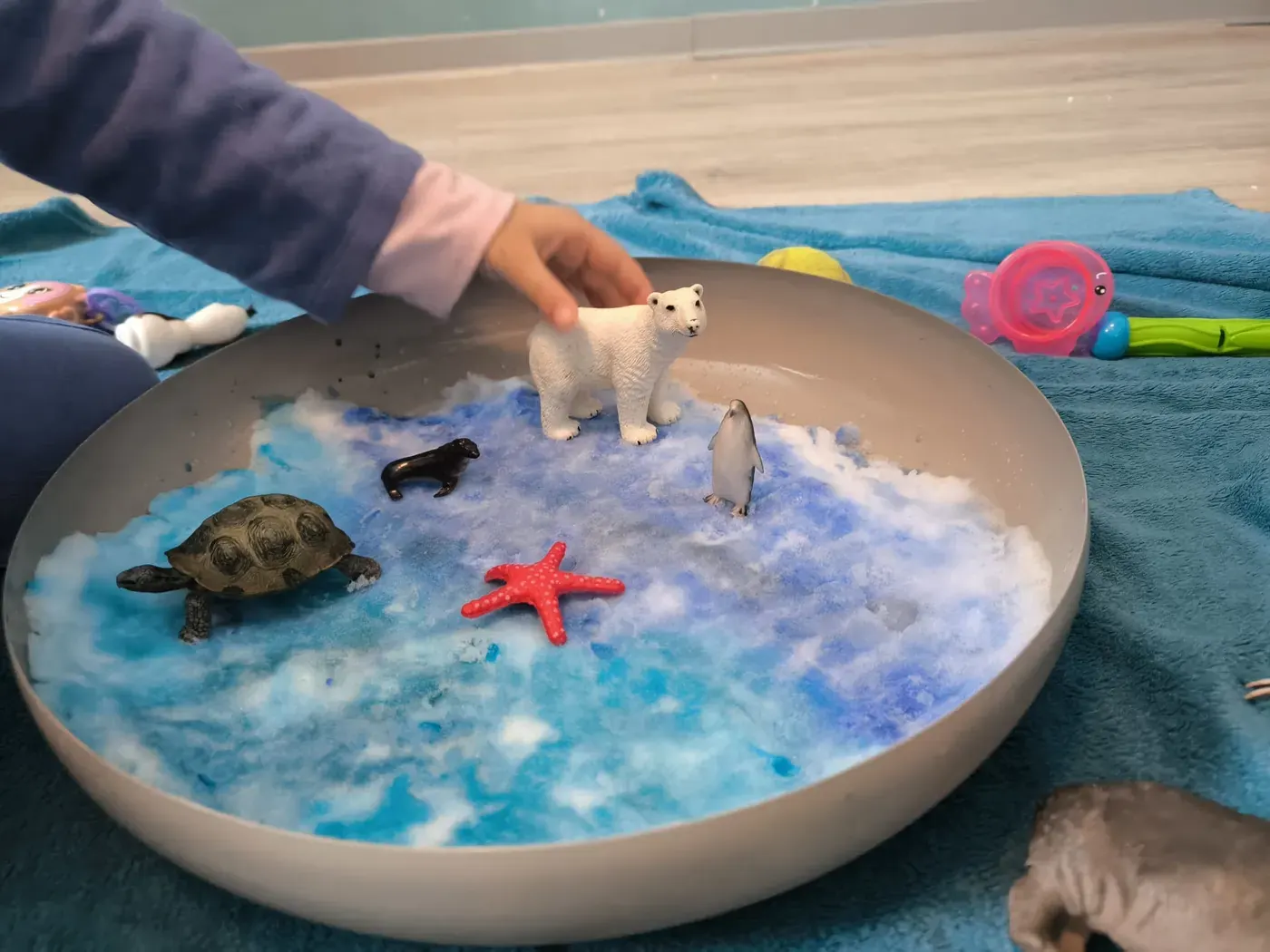 Kind spielt in der Ergotherapie mit Tierfiguren in einer Schale mit Meer-Landschaft
